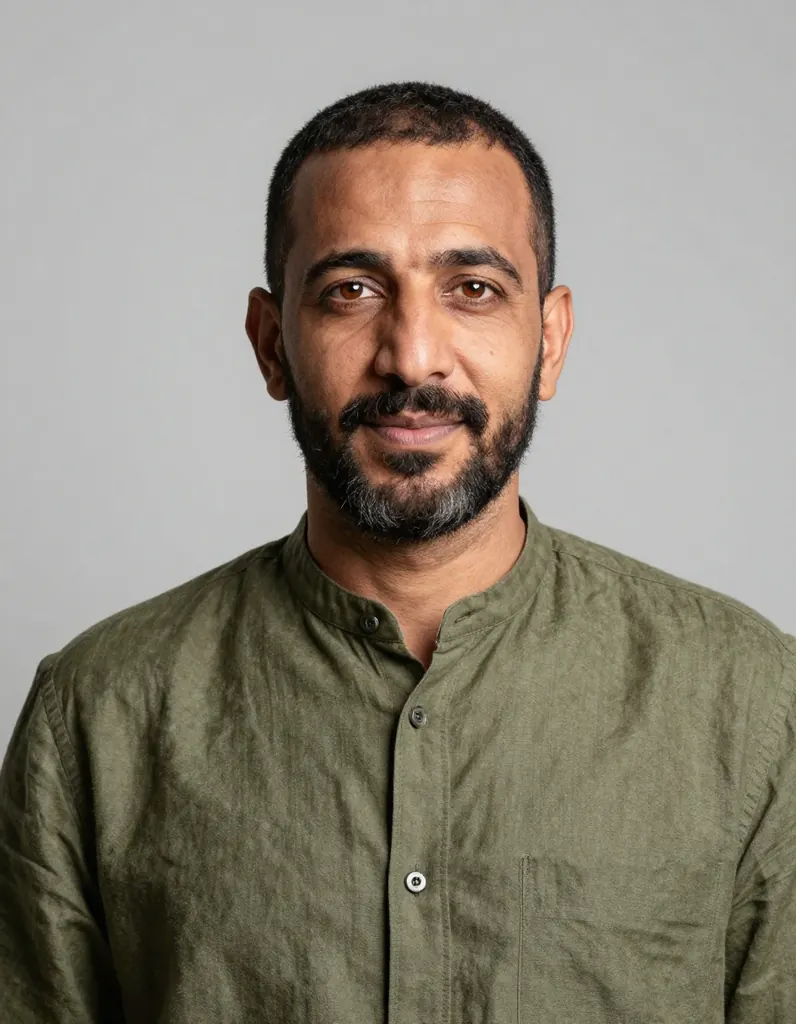 Crisp studio portrait of a Moroccan man in his late thirties with a short beard and warm brown eyes, wearing an olive linen shirt, clean light grey backdrop, soft key light and gentle rim light, sharp focus on the eyes, photorealistic